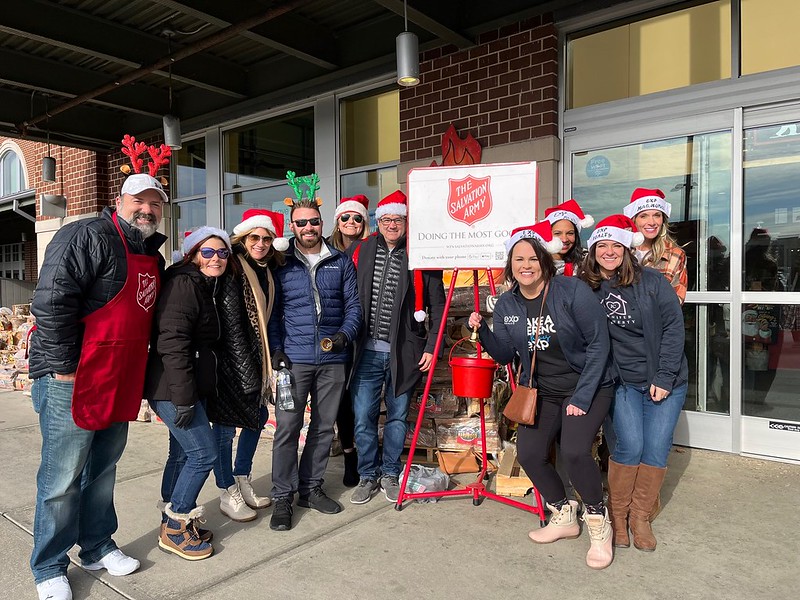 Realtors volunteering for the Salvation Army Red Kettle Campaign stand together next to a red kettle and sign