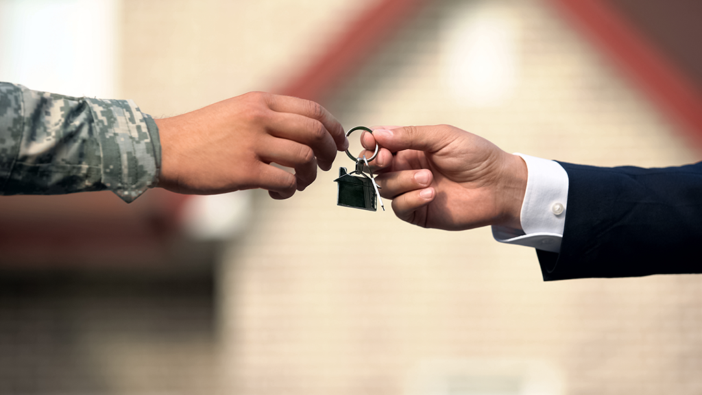 A person in business clothes hands a keychain to a person wearing a military uniform