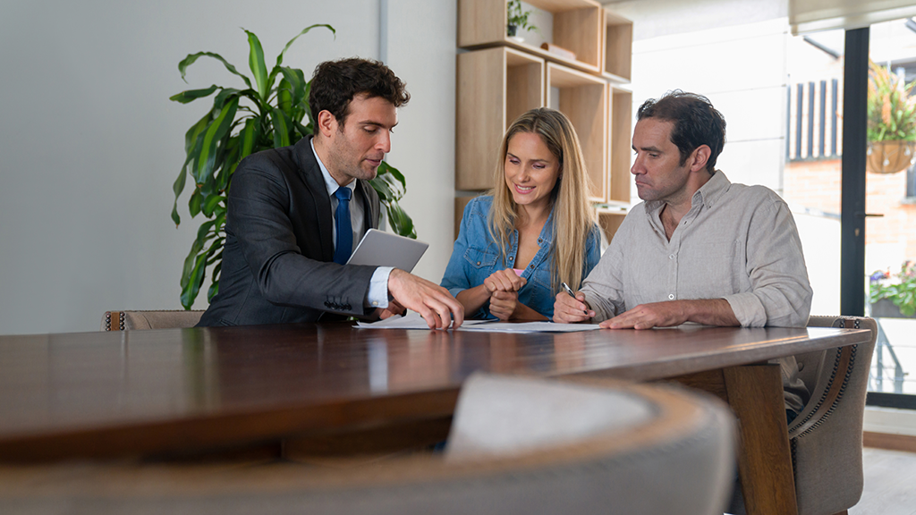 A businessman explains documents to a couple as they all sit inside a modern office