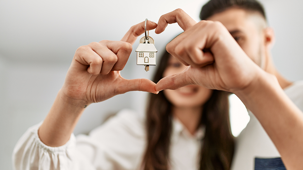 A couple holds keys as they form a heart with their fingers