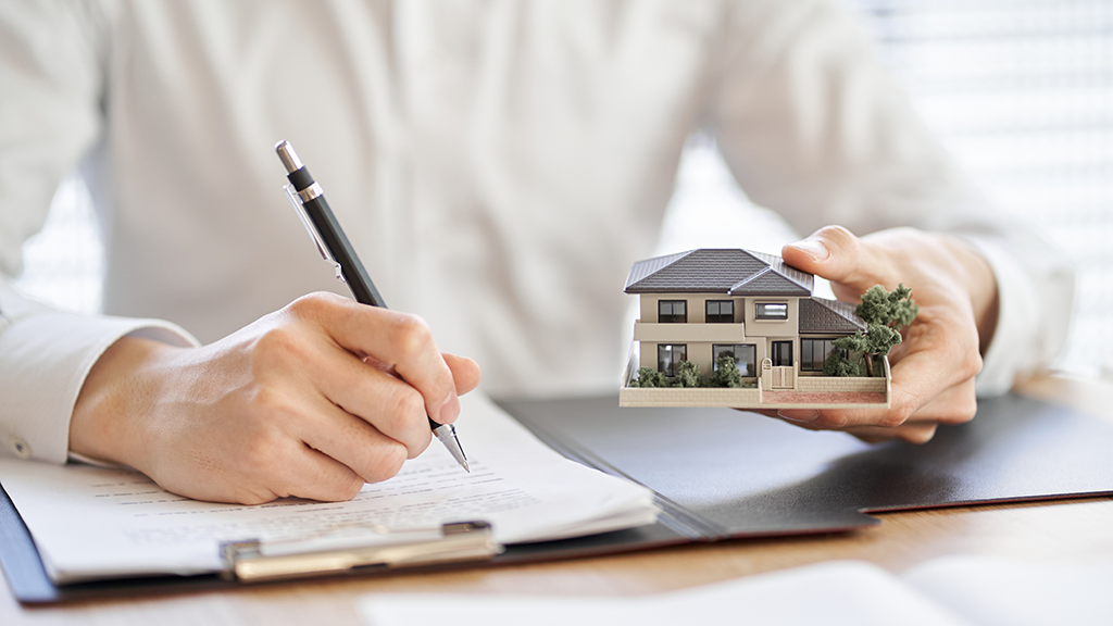 A person writing in a portfolio and holding a house figurine