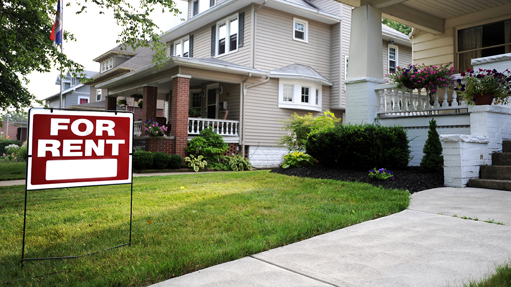 For rent sign in front of an apartment and other houses in the background