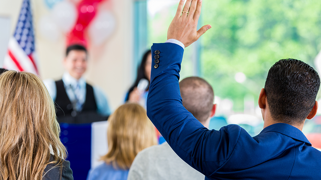 A man in the crowd raises his hand to ask a question