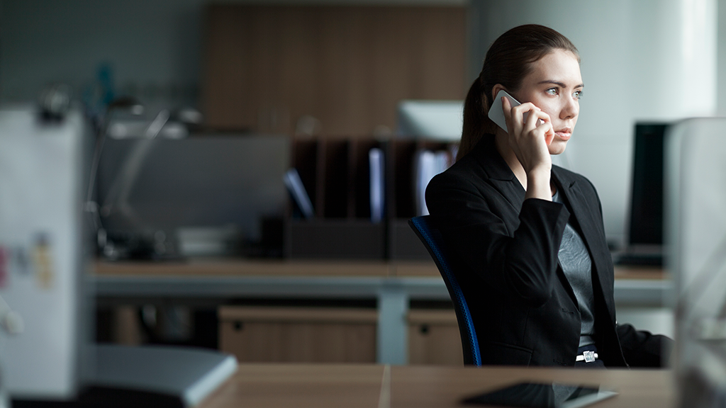 A woman looking serious sits in an office as she talks on the phone