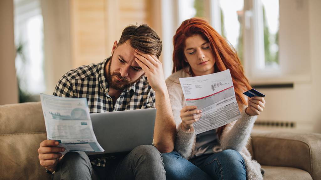 A couple look over financial documents together and have sad expressions on their faces